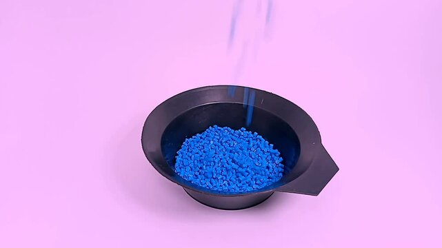Blue color masterbatch flowing contained in cup, various polymer masterbatch plastic granules carrying color pigment, isolated on pink background, for industrial plastic product videography design