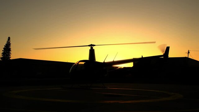 Silhouette of a helicopter with a rotating rotor in front of a sunset. Spinning propeller of aircraft engine closeup view. Scenic cinematic shot of helicopter prepared to fly during sinrise dawn