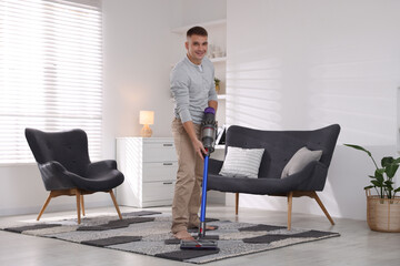 Young man cleaning rug with cordless vacuum cleaner at home © New Africa