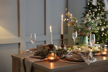Christmas table setting with stylish dishware, glasses and burning candles in festive decorated room