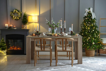 Christmas table setting with stylish dishware, glasses and burning candles in festive decorated room