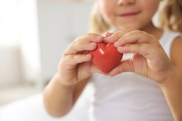 Orphanage concept. Little girl with red heart figure indoors, closeup