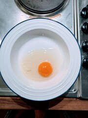 Raw egg in dish standing on stainless steel cooker hob