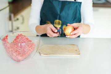 Woman cutting onions in the kitchen to prepare homemade cutlets