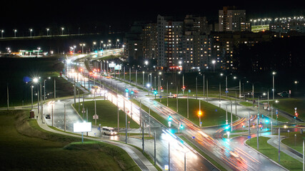Obraz premium Car traffic in the night city. Traces of light from the headlights on the street. Top view of the roadway near residential buildings. Slow motion, soft focus.