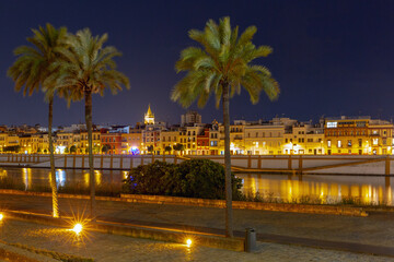 Nighttime view of the illuminated Triana district in Seville, Spain, showcasing its traditional...