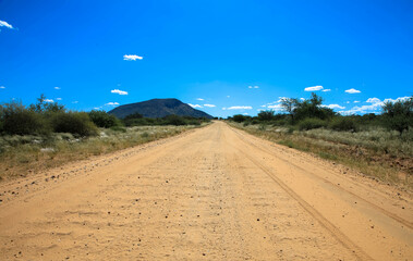 Endless and sandy gravel road through the desert in the beautiful Kalahari National Park. Tourism and vacation concept. Namibia, Africa.
