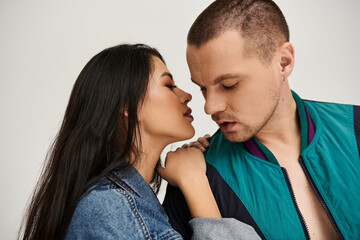 A beautiful young couple in stylish attire embraces intimately in a studio setting.