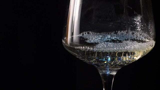 glass goblet filled with white wine on black background. close up