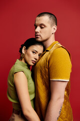A beautiful couple embraces, showcasing their fashionable outfits in a striking studio backdrop.