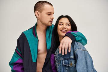 Young couple embraces with joy, showcasing their fashionable outfits in a studio backdrop.