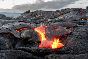 Lava field in Hawaii at dusk shows magma oozing through cracks in the earth and forming what will be new terrain.
