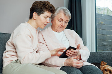A young woman explaining her senior mother or grandma how to use smartphone. Retired lady...