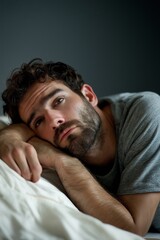 A young man lies thoughtfully on the bed, lost in reflection and emotion, capturing a moment of introspection.