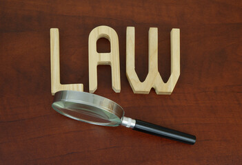 Letters law under magnifying glass on wooden table.