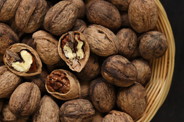 Walnuts in a wicker basket on a dark wooden background. Nuts in an oval basket, top view. Heap of walnuts in shells, close-up, background. Healthy eating. Harvest, agriculture