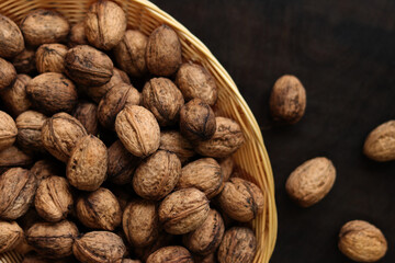 Walnuts in a wicker basket on a dark wooden background. Nuts in an oval basket, top view. Heap of walnuts in shells, close-up, background. Healthy eating. Harvest, agriculture