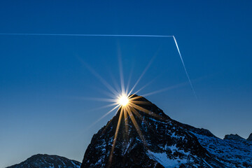 Sole al tramonto dietro alla montagna e scie di aerei