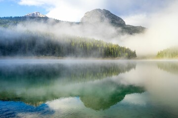 Serene mountain landscape with mist over a reflective lake, capturing the tranquility of nature.