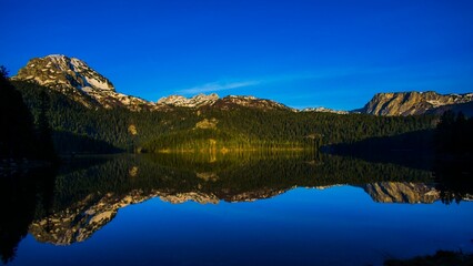 Fototapeta premium Serene mountain landscape with clear reflections on a tranquil lake under a vivid blue sky.