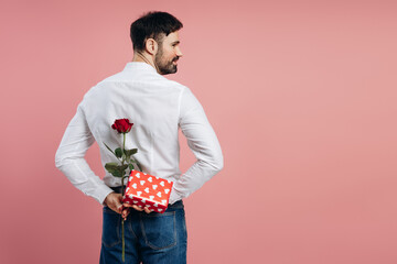 Man hiding red rose and valentine's day gift behind back copy space