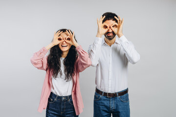 Cheerful couple mimicking glasses with fingers on white background