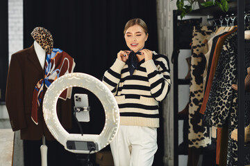 A stylish young woman films her outfit choices on her smartphone.