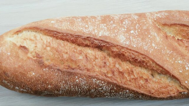Artisan quality of long loaf of bread covered in fine flour particles. Close-up slider shot of freshly baked French Baguette. Top down view. Food, Cuisine, Baking, Pastry, Home Baking, Rustic themes.
