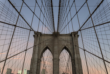Fototapeta premium Brooklyn Bridge close up detail looking up at suspension cables at sunrise (beautiful landmark travel tourism destination in NYC) iconic New York City attraction over east river downtown Manhattan USA