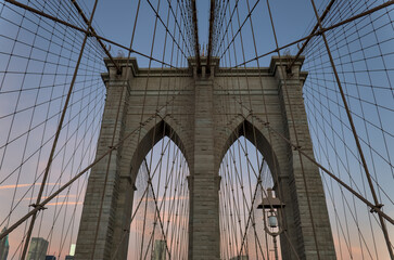 Fototapeta premium Brooklyn Bridge close up detail looking up at suspension cables at sunrise (beautiful landmark travel tourism destination in NYC) iconic New York City attraction over east river downtown Manhattan USA