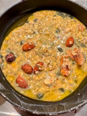 Raw egg omelette mixture in small frying pan with oats, nuts, seeds, cinnamon