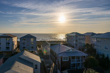 A beautiful sunrise over the Atlantic ocean with homes and condos, lush green trees, a sandy beach and ocean waves in Carolina Beach North Carolina USA