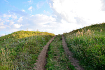 Obraz premium a dirty road is in the grass that is made by a single track going to the sky