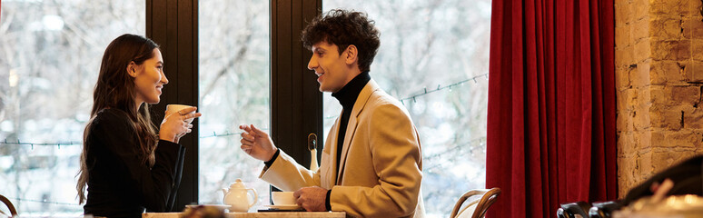 A couple shares a joyful moment, sipping drinks and laughing together in a romantic restaurant,...