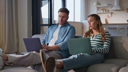 Fototapeta premium Talking pair working laptops at living room interior. Tired lady closing gadget