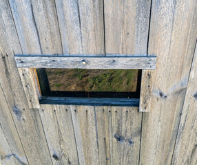 Close-up of a rustic wooden wall with a small window creating a unique perspective. The texture and colors of the wood add charm and character.