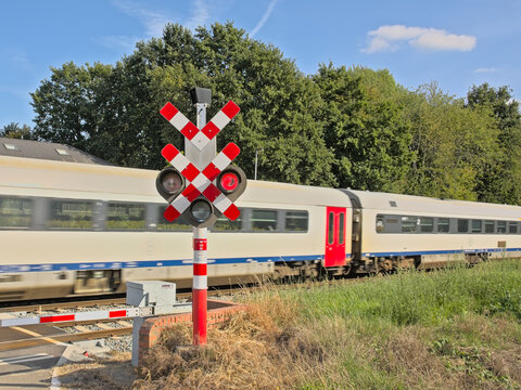 Passenger train with movement blur while passing a level crossing with red signaling light in the flemish countryside 