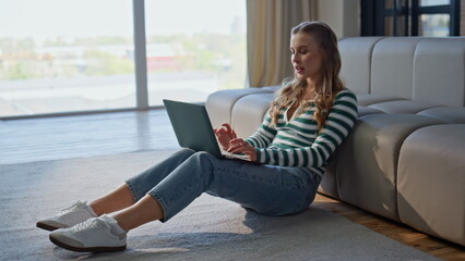 Thoughtful girl texting laptop in modern apartment. Pensive woman working online