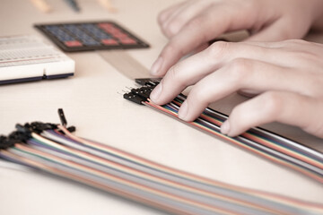Creating circuits using a solderless breadboard and wires. Hands working with a set of colorful jumper wires. Electronics or programming projects.