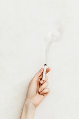 Hand Holding Cigarette with Smoke on Light Textured Background