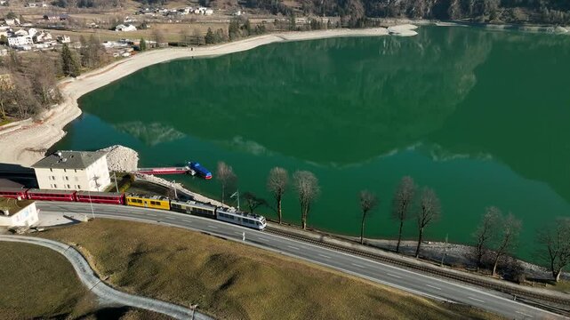 4k ujęcie z drona za jadącym pociągiem nad alpejskim jeziorem w Szwajcarii, Grudzień 2024