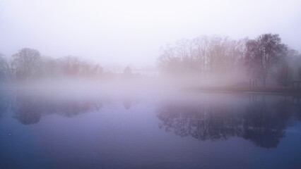 Fototapeta premium Foggy winter landscape with trees in the mist and snow-covered ice over the lake in New Haven, Connecticut, USA