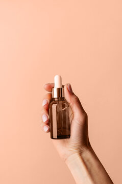 Dropper Bottle Mock-Up. Female hand holding amber glass dropper bottle on beige background