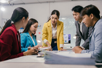 Group of asian businesspeople reviewing paperwork and discussing financial data during a productive meeting in a modern office