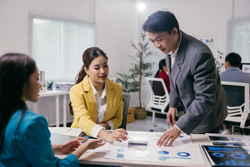 Three asian businesspeople are having a meeting in a modern office, analyzing charts and reports together, working collaboratively on a project