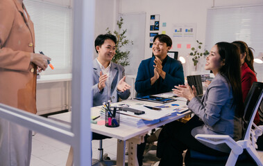 Asian businesspeople are clapping their hands after a successful presentation by a female executive in a modern office, celebrating achieving their business goals