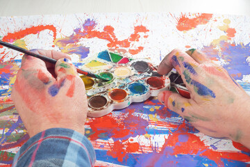 Obraz premium The photo shows the artist's hands with a brush for painting, against a background of watercolor paints