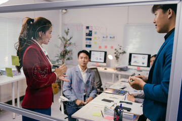 Fototapeta premium Diverse business team collaborating on glass board in modern office, strategizing for new project with focus on innovation and teamwork. Goal: achieve success through effective collaboration