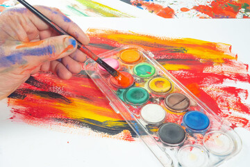 Obraz premium The photo shows the artist's hands with a brush against a background of watercolor paints.