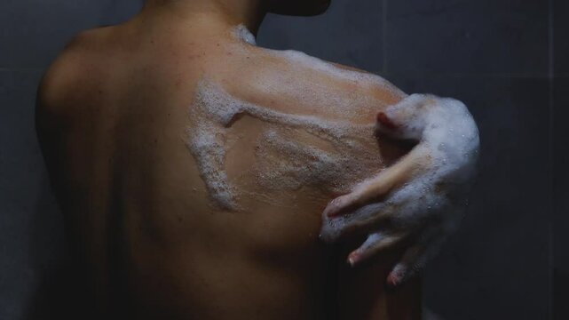 Skinny woman with problem skin on her back soaps her shoulder in shower